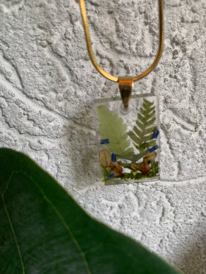 Necklace With rectangular pendant containing ferns, lavender and leaves.